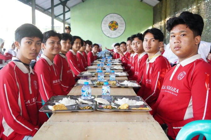 Para peserta Bela Negara Mahasiswa Universitas Negeri Malang (UM) duduk bersama menikmati makan pagi di meja panjang, terlihat akrab dan penuh semangat