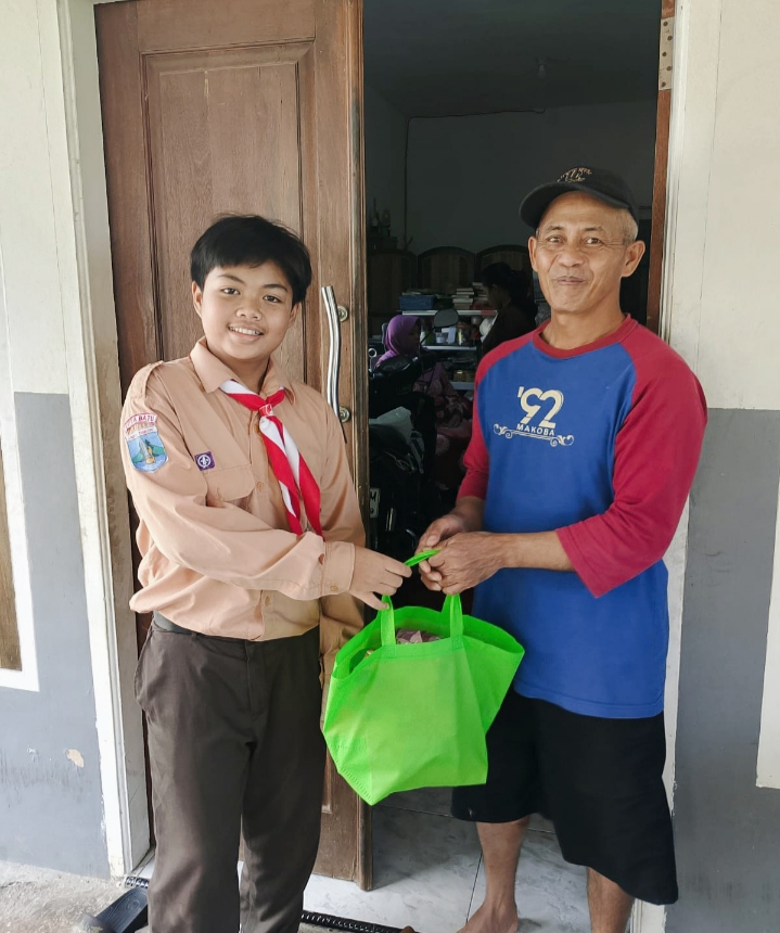 Siswa kelas 6 MI Miftahul Ulum dengan bersuka cita memberikan paket sembako, tampak seoarang bapak menerimanya dengan senang. 