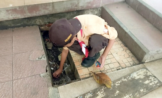 Tampak salah satu siswa membersihkan saluran air di area sekolah dari sampah